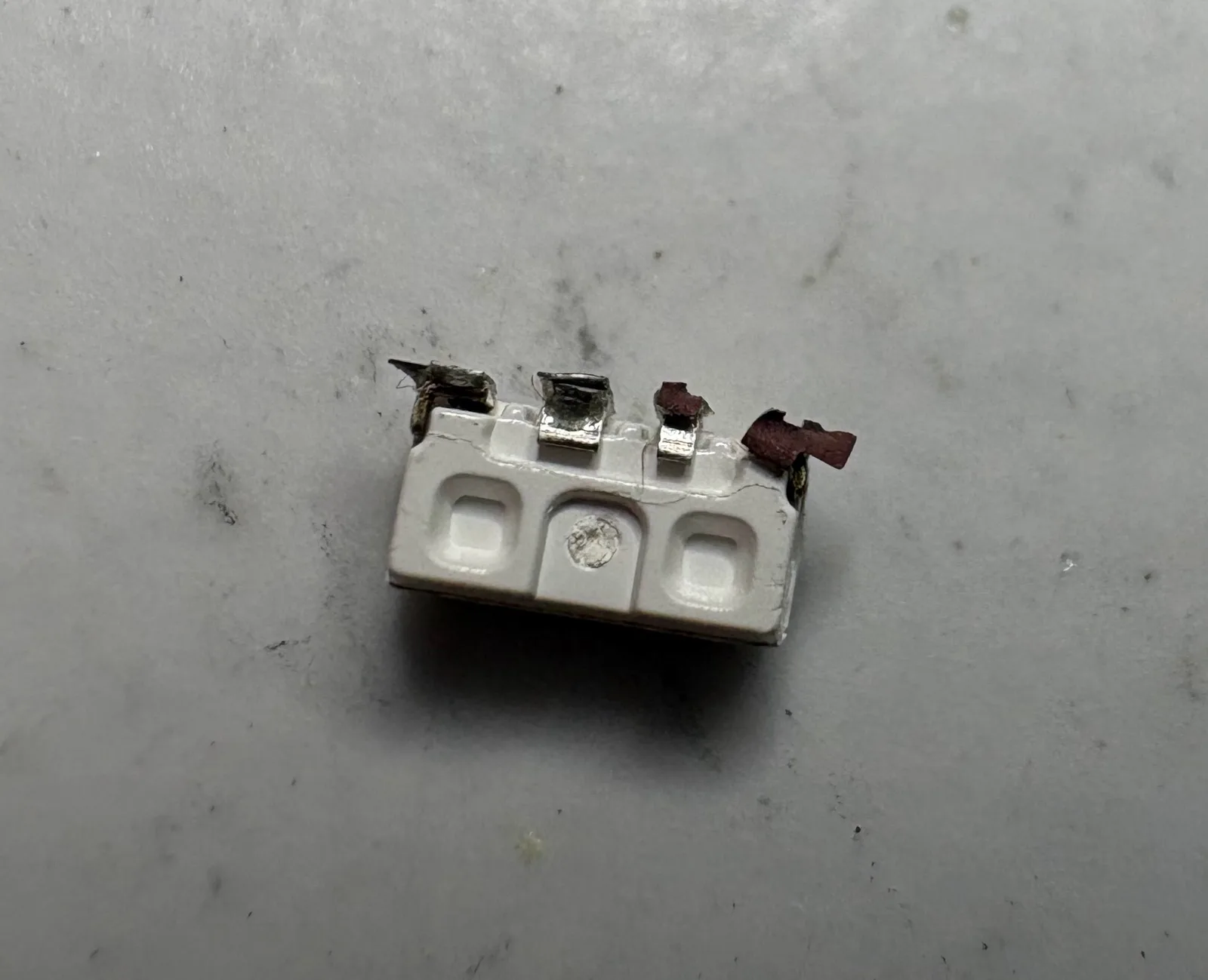 The torn-off LED on a light surface, all four copper pads still attached to its terminals.