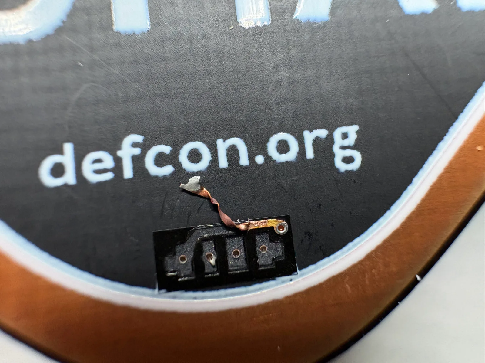 Closeup of the badge PCB where the LED was torn away. Four bare vias sit in the black footprint, with a copper trace and one dangling pad above it.