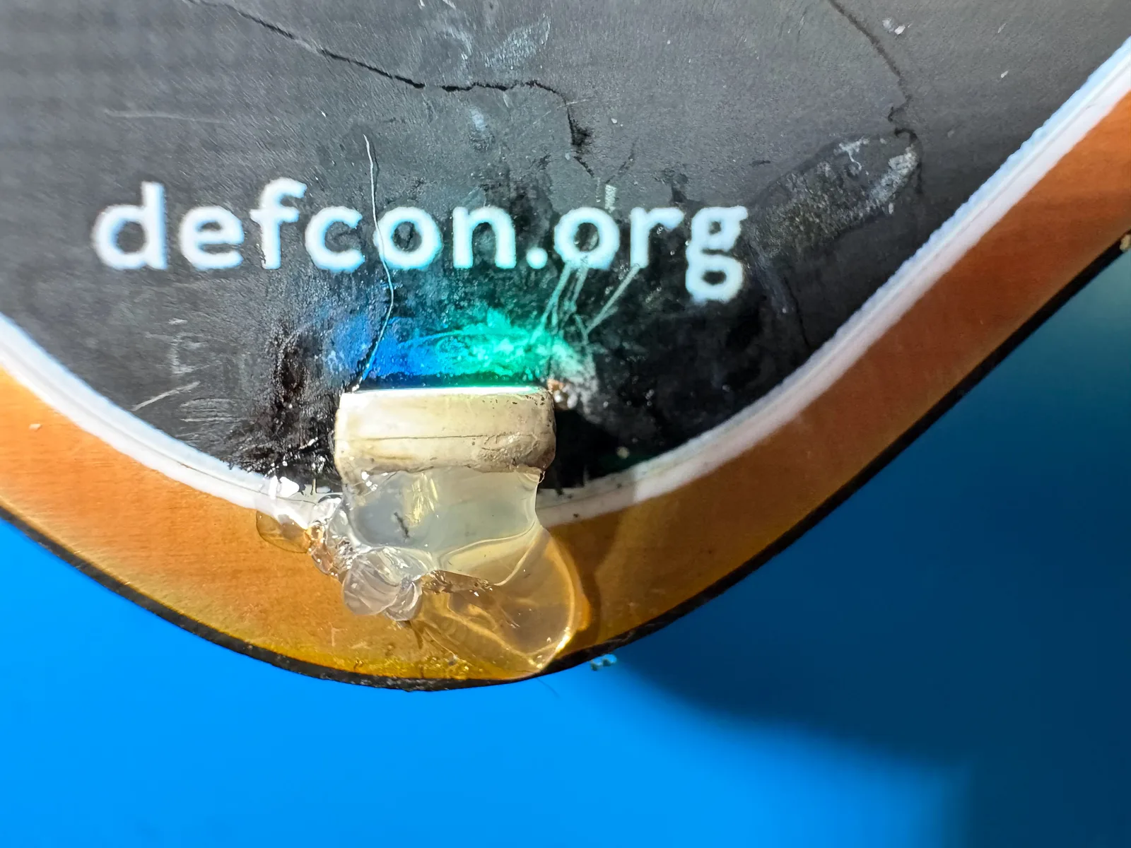 The repaired LED in place on the badge edge, lit green-blue, held down by a blob of hot glue.