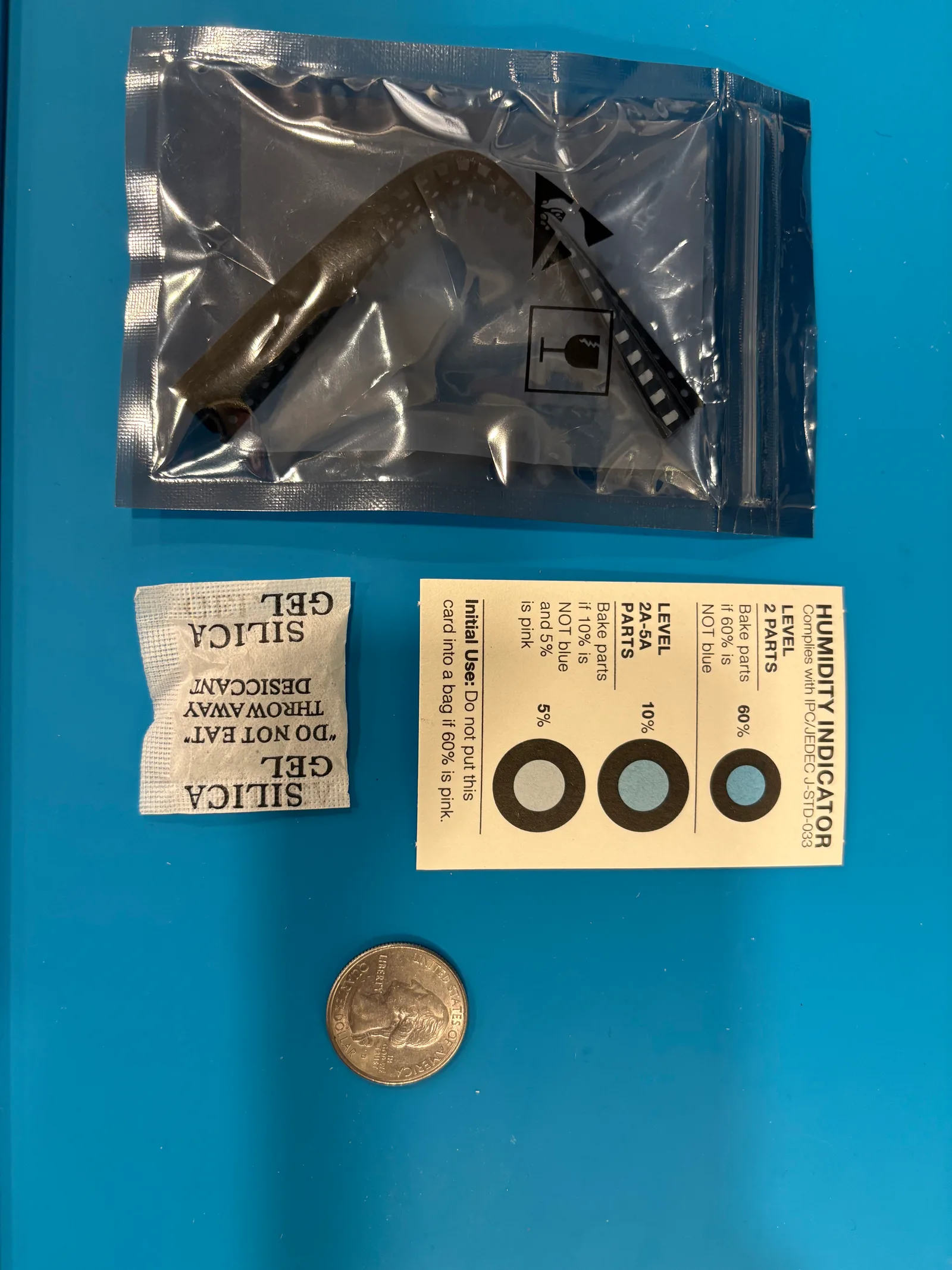 An anti-static bag holding the coiled carrier strip, next to a silica gel packet and a humidity indicator card.